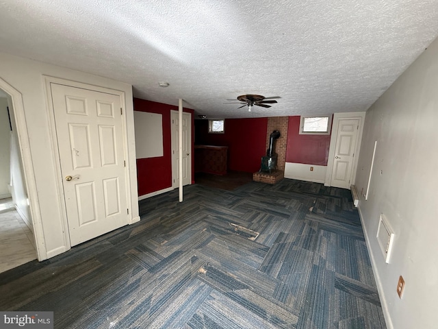 interior space featuring a wood stove, ceiling fan, and a textured ceiling