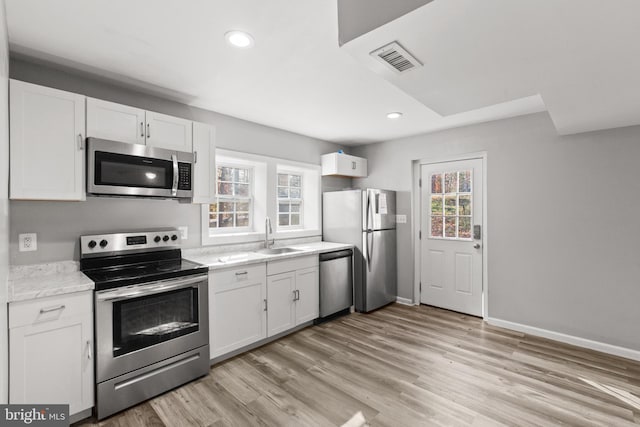 kitchen featuring sink, light stone counters, light hardwood / wood-style flooring, white cabinets, and appliances with stainless steel finishes