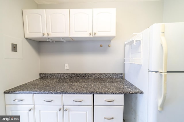 kitchen featuring white cabinets, white refrigerator, and dark stone counters