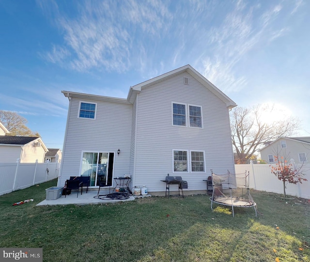 back of house featuring a lawn, a patio, and a trampoline