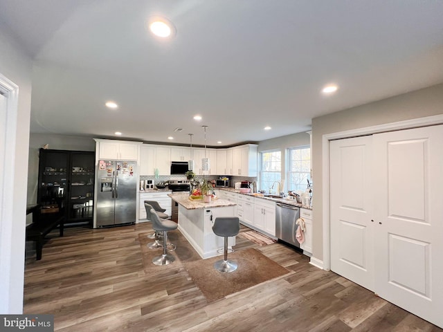 kitchen with a center island, hanging light fixtures, stainless steel appliances, dark hardwood / wood-style floors, and a breakfast bar area