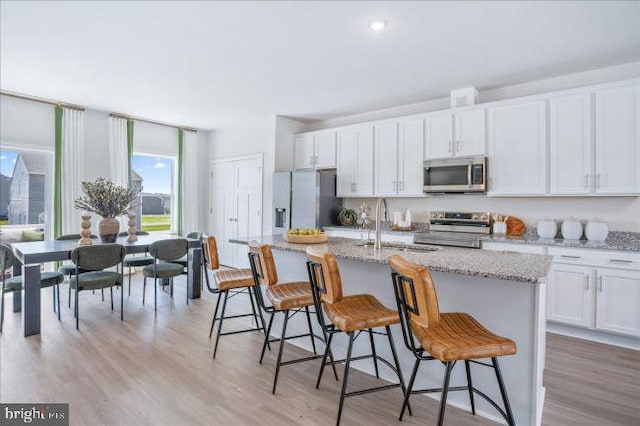 kitchen featuring a kitchen bar, stainless steel appliances, a center island with sink, light hardwood / wood-style floors, and white cabinetry