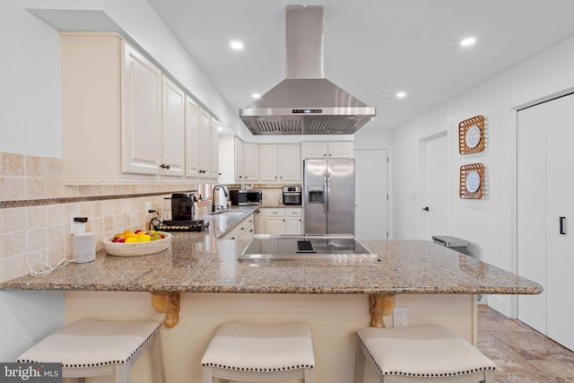 kitchen with a kitchen bar, appliances with stainless steel finishes, kitchen peninsula, and range hood