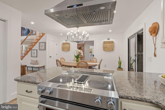 kitchen with dark stone countertops, white cabinetry, stove, and wall chimney range hood