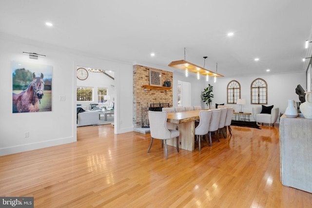 dining room featuring a brick fireplace, light hardwood / wood-style flooring, and ornamental molding