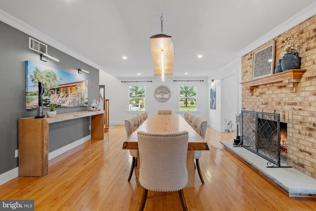 dining area with a brick fireplace, crown molding, and light hardwood / wood-style flooring