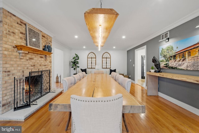 dining area with a brick fireplace, light hardwood / wood-style flooring, and crown molding