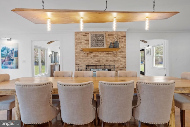 dining area with hardwood / wood-style flooring, a healthy amount of sunlight, crown molding, and a brick fireplace