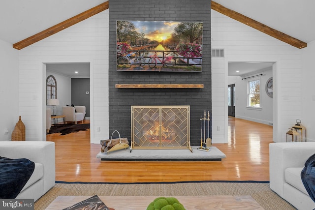 living room featuring a fireplace, beam ceiling, light wood-type flooring, and high vaulted ceiling