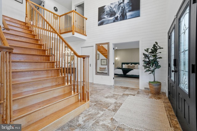 foyer featuring french doors, a towering ceiling, and wooden walls