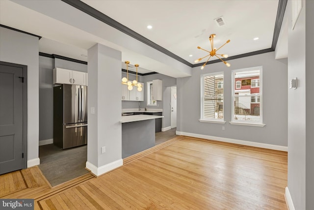 unfurnished living room with an inviting chandelier, crown molding, and light wood-type flooring