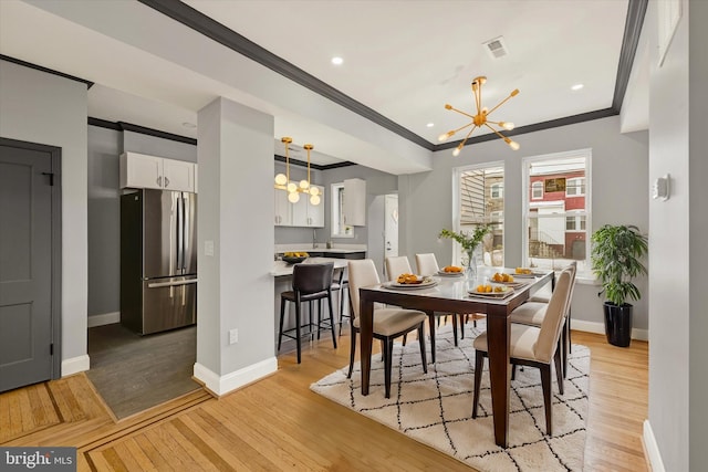 dining area with an inviting chandelier, ornamental molding, and light wood-type flooring