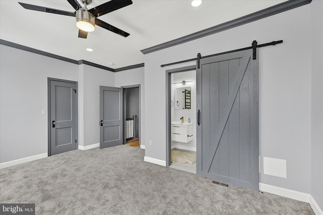 unfurnished bedroom with carpet, connected bathroom, ceiling fan, crown molding, and a barn door