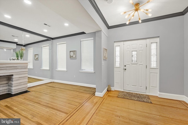 entrance foyer featuring a fireplace, a notable chandelier, crown molding, and hardwood / wood-style floors