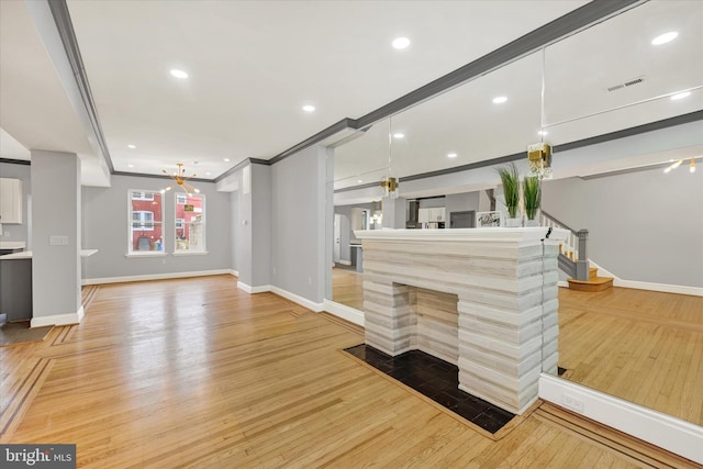 unfurnished living room with light wood-type flooring, a multi sided fireplace, and crown molding