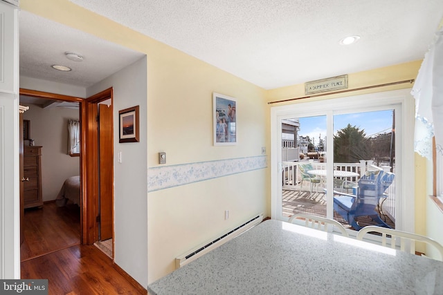 hall with a textured ceiling, dark wood-type flooring, and a baseboard heating unit