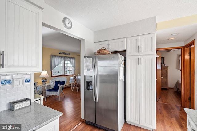 kitchen with stainless steel fridge, light wood-type flooring, backsplash, light stone counters, and white cabinets