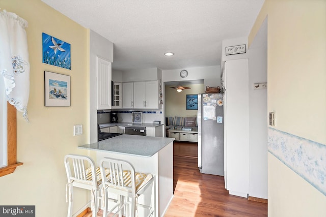 kitchen with dark wood-type flooring, white cabinets, stainless steel fridge, a kitchen bar, and kitchen peninsula