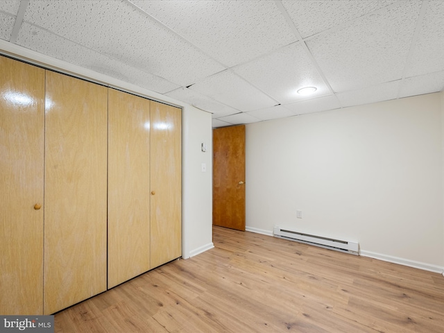 unfurnished bedroom featuring a baseboard radiator, light hardwood / wood-style floors, a paneled ceiling, and a closet