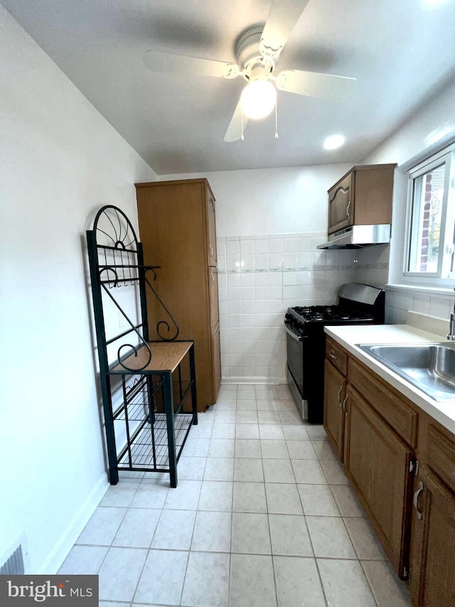 kitchen with black gas range, sink, ceiling fan, light tile patterned floors, and tile walls