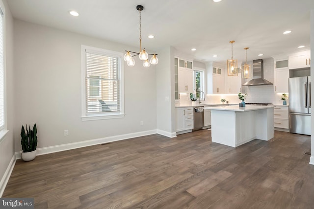 kitchen with a center island, white cabinets, wall chimney range hood, hanging light fixtures, and appliances with stainless steel finishes