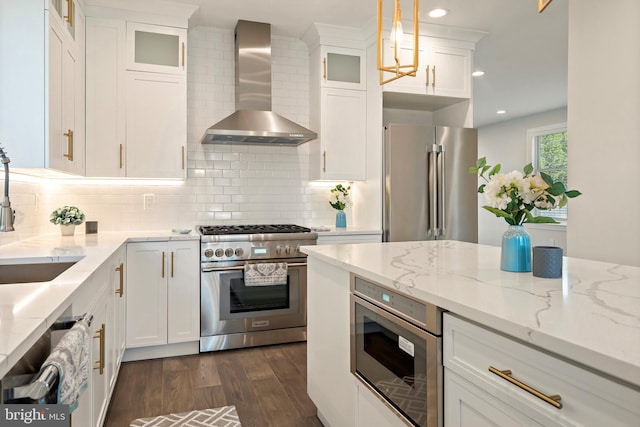 kitchen featuring white cabinets, premium appliances, decorative light fixtures, and wall chimney exhaust hood