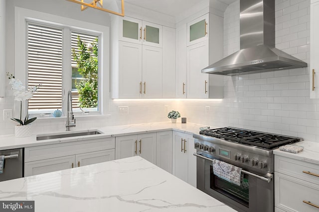 kitchen with decorative backsplash, appliances with stainless steel finishes, light stone counters, wall chimney exhaust hood, and sink