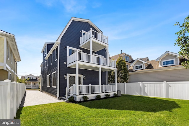 rear view of house with covered porch, a balcony, and a yard