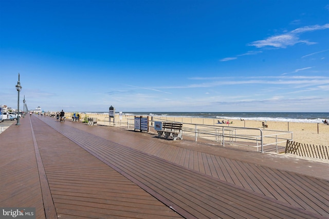 wooden terrace featuring a water view and a beach view