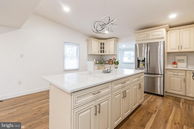 kitchen featuring stainless steel fridge with ice dispenser, backsplash, cream cabinets, light hardwood / wood-style floors, and a kitchen island