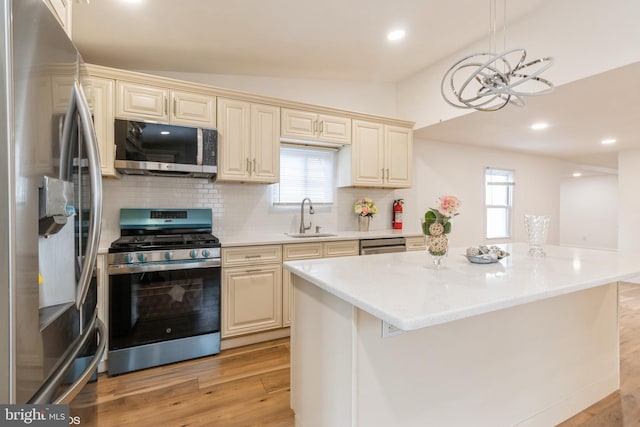 kitchen featuring cream cabinets, sink, hanging light fixtures, light wood-type flooring, and stainless steel appliances