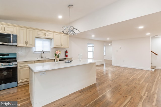 kitchen featuring sink, stainless steel appliances, cream cabinets, decorative light fixtures, and a kitchen island