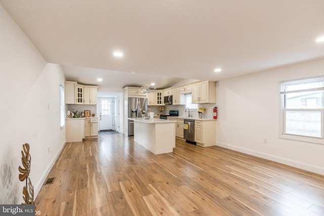 kitchen with cream cabinets, an island with sink, light wood-type flooring, decorative backsplash, and appliances with stainless steel finishes