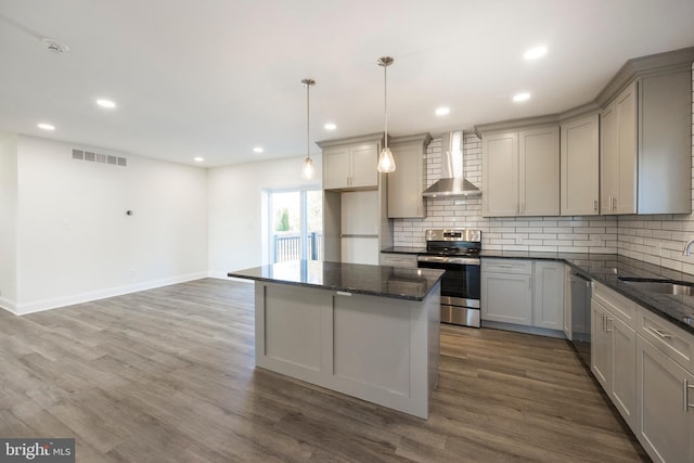 kitchen with gray cabinetry, wall chimney range hood, dark hardwood / wood-style flooring, pendant lighting, and appliances with stainless steel finishes