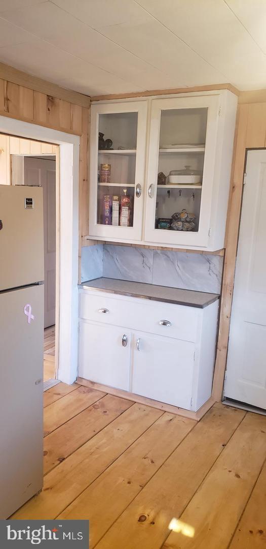 kitchen with white cabinets, white fridge, light hardwood / wood-style floors, and wooden walls