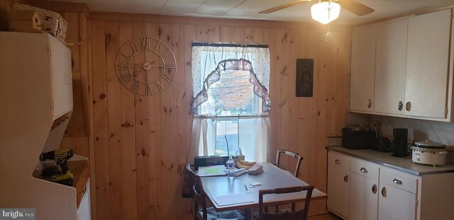 interior space with white cabinets, ceiling fan, and wooden walls