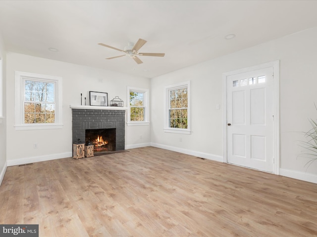 unfurnished living room with a fireplace, ceiling fan, plenty of natural light, and light hardwood / wood-style flooring