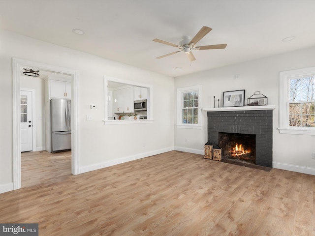 unfurnished living room with ceiling fan, a fireplace, and light hardwood / wood-style floors