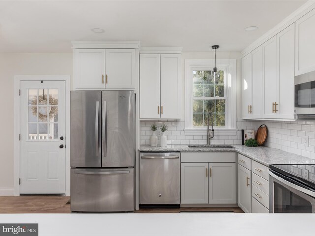 kitchen featuring appliances with stainless steel finishes, tasteful backsplash, sink, white cabinetry, and hanging light fixtures