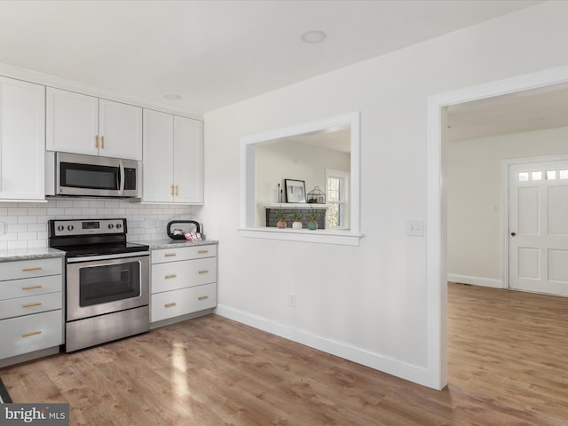 kitchen featuring light stone countertops, white cabinetry, light wood-type flooring, and appliances with stainless steel finishes