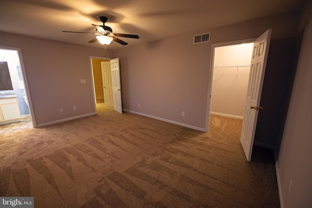 unfurnished bedroom with carpet flooring, a walk in closet, ensuite bathroom, ceiling fan, and a closet