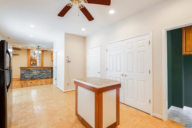 kitchen featuring tile counters, ceiling fan, black refrigerator, and light parquet flooring