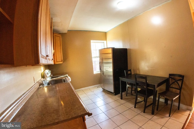 kitchen featuring brown cabinets, dark countertops, a sink, stainless steel fridge, and baseboards