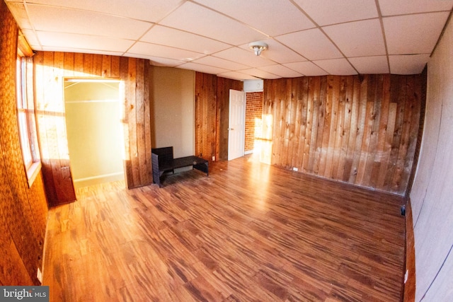 unfurnished living room featuring a drop ceiling, wooden walls, and wood finished floors