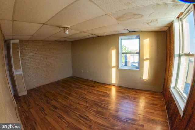 empty room with brick wall, wood finished floors, and a paneled ceiling