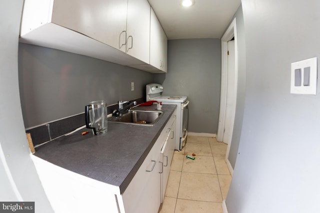 kitchen with dark countertops, white cabinets, light tile patterned flooring, a sink, and washer / dryer