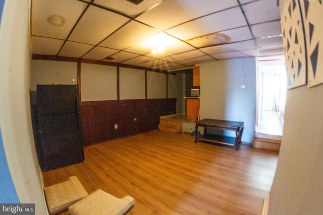 below grade area featuring a paneled ceiling, light wood-style flooring, and freestanding refrigerator