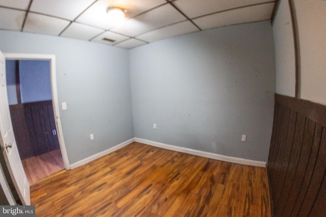 empty room with a paneled ceiling, baseboards, and wood finished floors