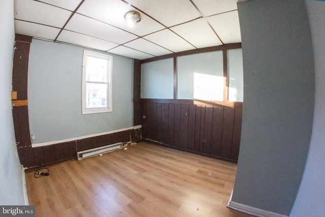 empty room with a wainscoted wall, a paneled ceiling, light wood-style flooring, baseboard heating, and wood walls