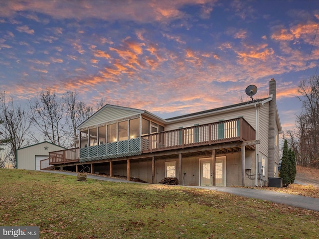 back house at dusk featuring central AC, a sunroom, a yard, and a deck